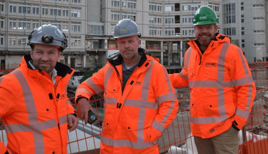Drie medewerkers van Bosman BAM Combinatie (BBC) in oranje veiligheidsjassen op de bouwplaats van de grootschalige revitalisatie van het ABN AMRO-kantoor aan de Foppingadreef in Amsterdam.
