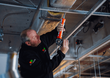 Een leidinggevend monteur van Bosman Bedrijven werkt aan installaties in een plafond.