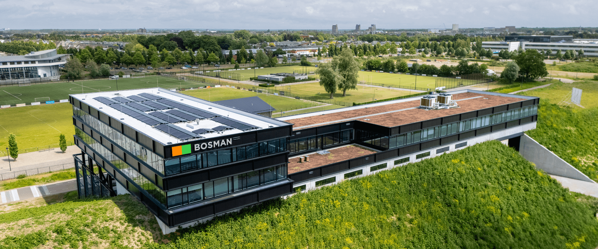 Achterzijde van het nieuwe Bosman-kantoor langs de A1 bij Amersfoort, met grote glaspartijen en uitzicht op de snelweg vanaf een verhoogde geluidswal.