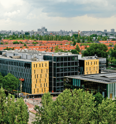 Buitenaanzicht van EDGE Stadium in Amsterdam, een modern en duurzaam kantoorgebouw met glazen gevels en gele accenten, omringd door groen.