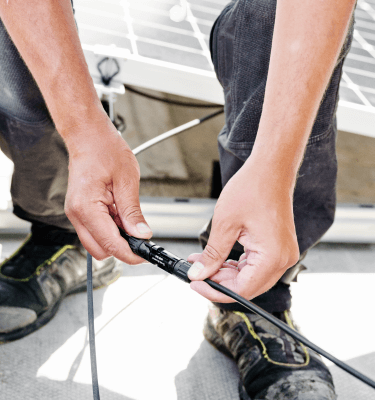 Handen van een technicus die kabels aansluiten, met werkschoenen zichtbaar op de achtergrond.