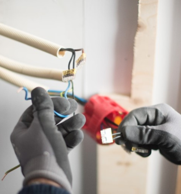 Elektricien met handschoenen werkt veilig aan elektrische bedrading, symbool voor vakmanschap en veiligheid in installatietechniek.