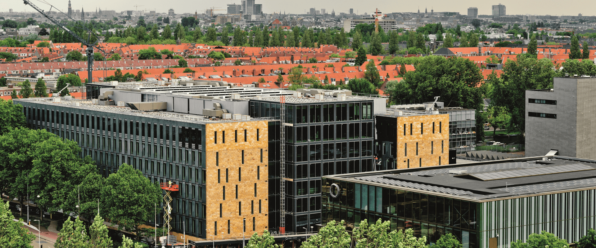 Buitenaanzicht van EDGE Stadium in Amsterdam, een modern en duurzaam kantoorgebouw met glazen gevels en gele accenten, omringd door groen.