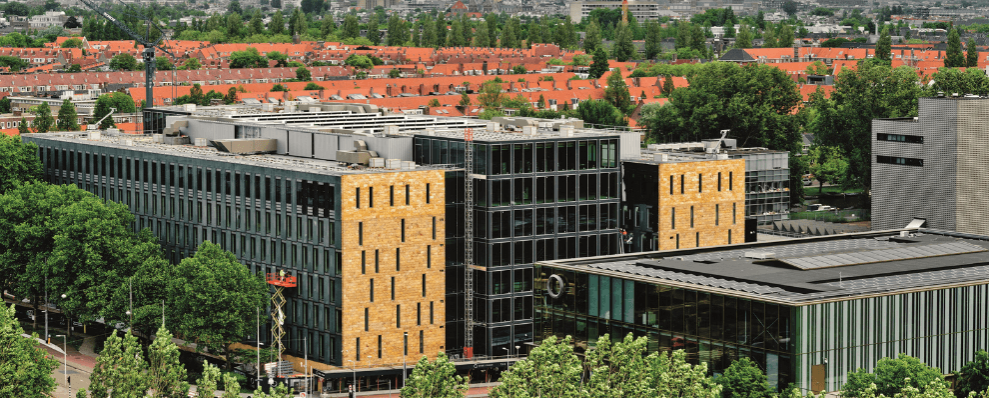 Buitenaanzicht van EDGE Stadium in Amsterdam, een modern en duurzaam kantoorgebouw met glazen gevels en gele accenten, omringd door groen.