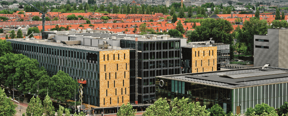 Buitenaanzicht van EDGE Stadium in Amsterdam, een modern en duurzaam kantoorgebouw met glazen gevels en gele accenten, omringd door groen.