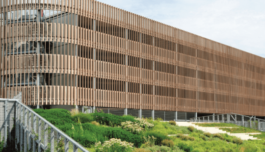 P+R Genneper Parken in Eindhoven, een duurzaam ontworpen parkeergarage met een houten gevel en groene daken, geïntegreerd in een natuurlijke omgeving.