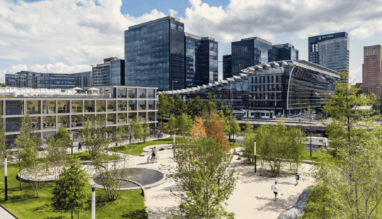 Het Strawinskyhuis in Amsterdam, een modern en duurzaam kantoorgebouw aan de Zuidas, omringd door groen en met een levendige stadsskyline op de achtergrond.
