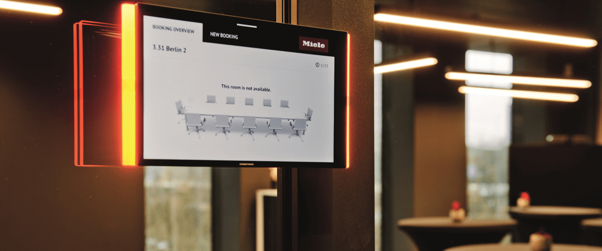 Digitaal reserveringsscherm voor een vergaderruimte bij Miele X in Amsterdam, gemonteerd op een zwarte pilaar in een modern kantoorinterieur.