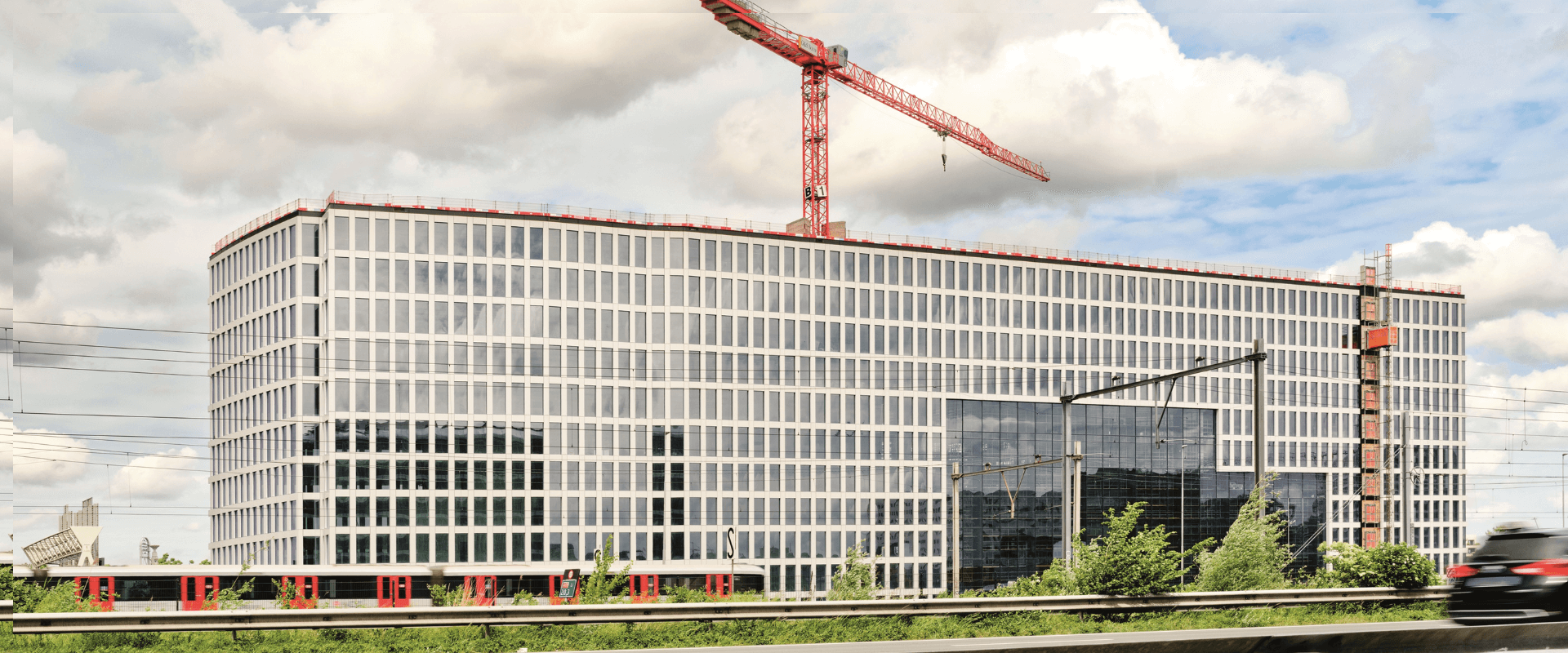 Bouw van Tripolis Park in Amsterdam, een modern en duurzaam kantoorgebouw met glazen gevel en rode bouwkraan op de achtergrond.