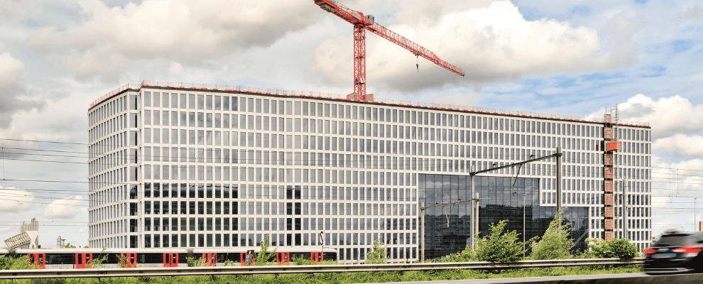 Bouw van Tripolis Park in Amsterdam, een modern en duurzaam kantoorgebouw met glazen gevel en rode bouwkraan op de achtergrond.