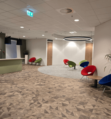 Moderne en sfeervolle ontvangstruimte met een receptiebalie, kleurrijke designstoelen en warme houten vloer, ontworpen voor een uitnodigende en comfortabele werkomgeving.