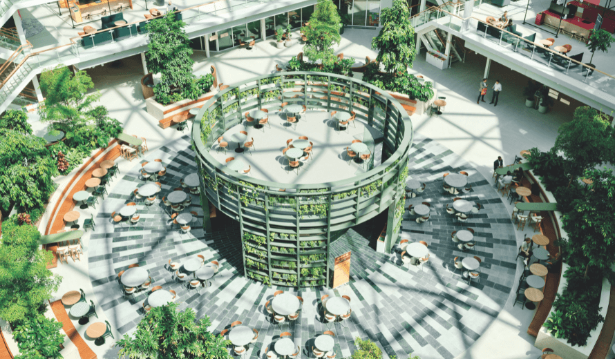 Licht en ruim atrium van EDGE Amsterdam West met groen begroeide centrale structuur, omringd door zitplaatsen en een glazen dakconstructie.