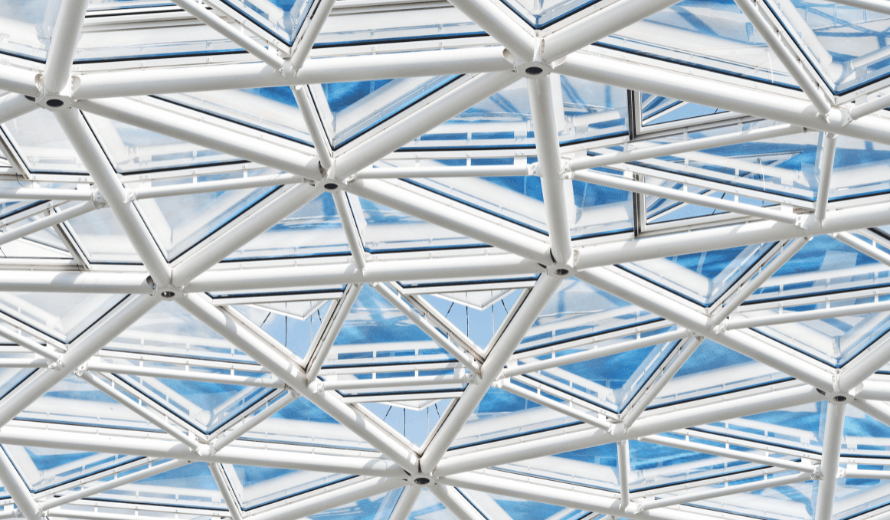 Glazen dakconstructie van het atrium in EDGE Amsterdam West, met witte stalen driehoekige raamkozijnen en doorkijk naar de blauwe lucht.