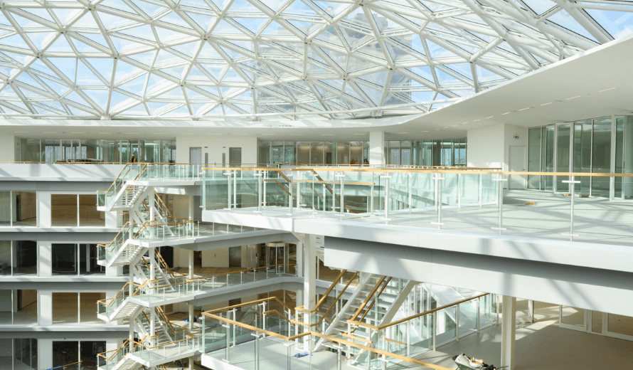 Ruim en licht atrium in EDGE Amsterdam West met glazen koepeldak, open trappen en transparante balustrades.