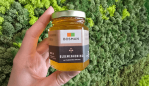 Hand houdt een pot Bosman bloemenhoning vast voor een groene moswand.