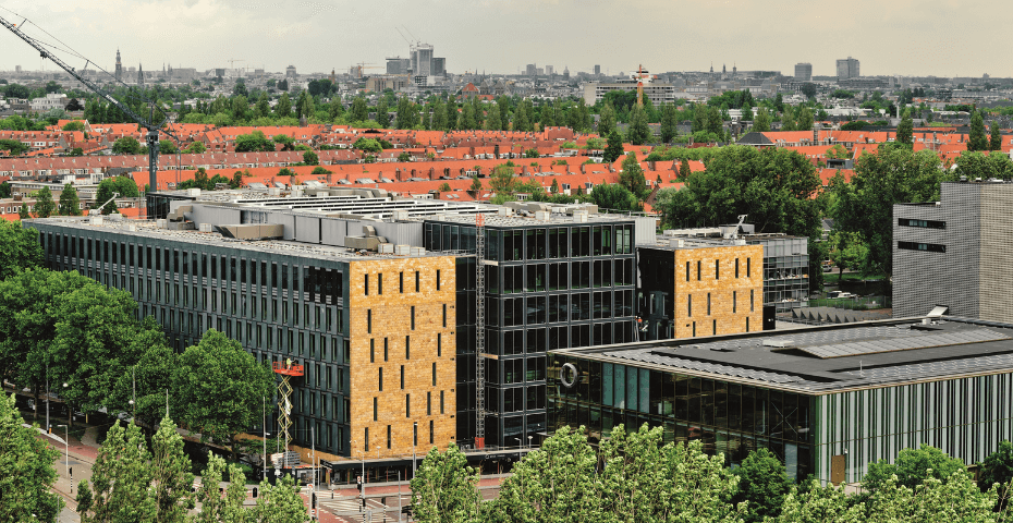 Buitenaanzicht van EDGE Stadium in Amsterdam, een modern en duurzaam kantoorgebouw met glazen gevels en gele accenten, omringd door groen.