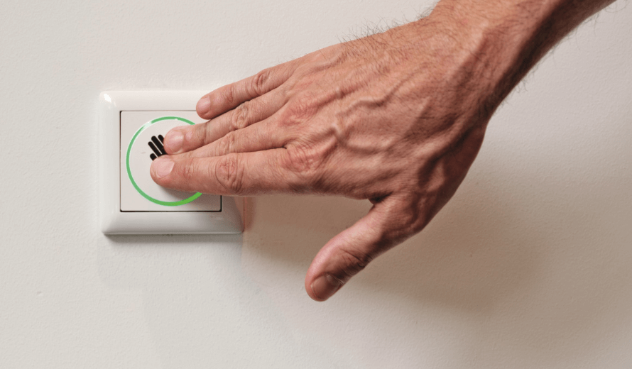 Hand drukt op een sensor met handpictogram en groene lichtcirkel aan de muur.