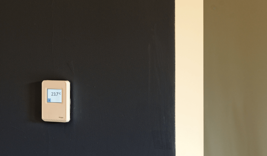 Digitale thermostaat op een donkerblauw geverfde muur met temperatuurweergave van 23,7 graden Celsius