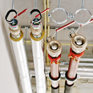 Detail van een technische installatie aan het plafond van het Gaudi-gebouw, met vier leidingen in isolatiemateriaal en ophangbeugels. De leidingen zijn zorgvuldig afgemonteerd en voorbereid voor aansluiting.